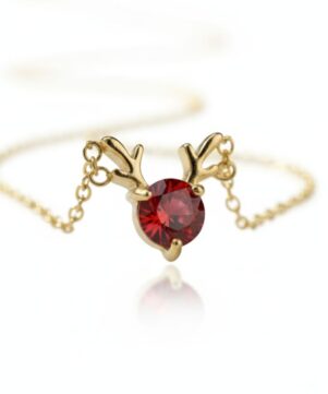 The ‘Noel’ Reindeer Antler Pendant Necklace cruve chain Close-up of a gold reindeer antler pendant necklace with a brilliant red cubic zirconia stone, on a white background with a subtle reflection.