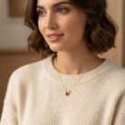 Model wearing a delicate gold reindeer antler pendant necklace with a red cubic zirconia stone, showing the necklace size against the collarbone